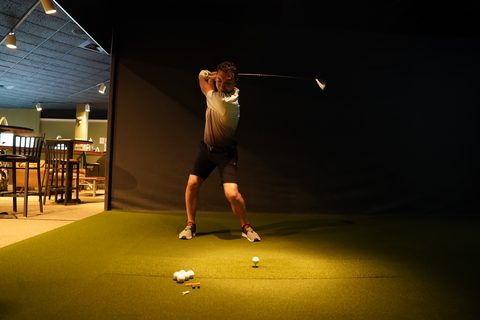A golfer at the top of the backswing in a Westborough bay, the lounge lit behind